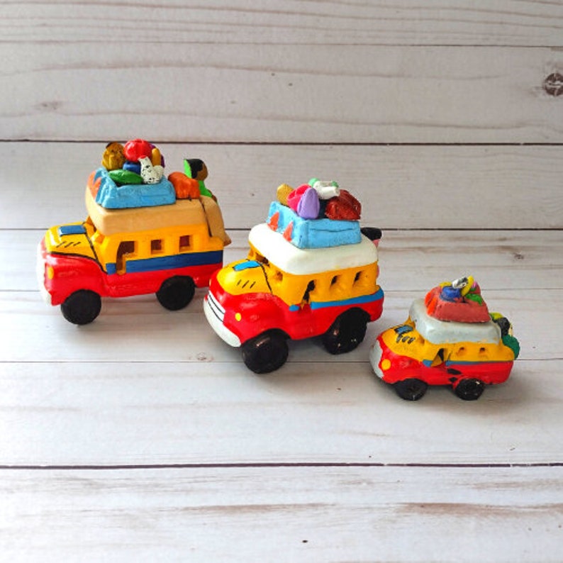 May include: Three colorful toy buses with passengers and luggage. The buses are made of clay and painted in bright colors, including red, yellow, blue, and green. The buses are arranged in a row from largest to smallest.
