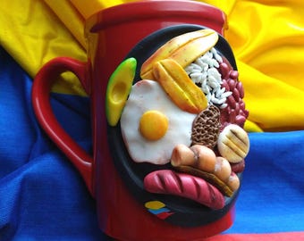 May include: Red ceramic mug with a 3D design of a Colombian breakfast dish, including fried plantains, rice, beans, avocado, fried egg, sausage, and arepas.