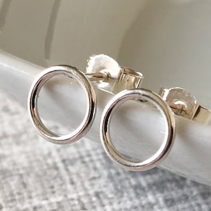 May include: A pair of silver circle stud earrings. The earrings are small and delicate, and they are perfect for everyday wear.