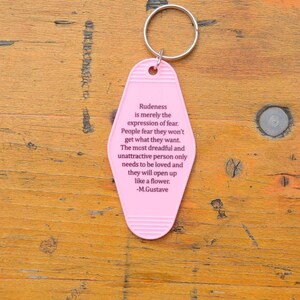 May include: Pink motel key chain with a quote about rudeness being an expression of fear. The quote is attributed to M. Gustave.
