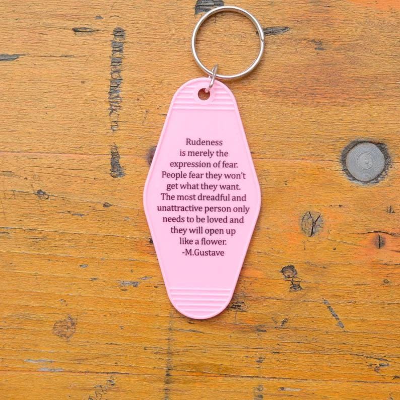 May include: Pink motel key chain with a quote about rudeness being an expression of fear. The quote is attributed to M. Gustave.