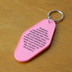 May include: Pink motel key chain with a quote about rudeness being an expression of fear. The quote is attributed to M. Gustave.