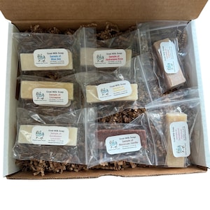 May include: A box filled with brown packing paper and ten small clear plastic bags containing bars of goat milk soap. Each bar has a label with the text "Goat Milk Soap" and the scent of the soap. The scents include Blue Sea, Hydrangea Rose, Cinnapear, Eucalyptus Lavender, and Moroccan Vanilla.