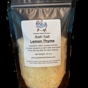 May include: A resealable plastic bag filled with bath salts. The label reads "Pampered Chelsea Products Bath Salt Lemon Thyme" and includes directions for use, net weight (16 ozs), and ingredients: Epsom Salt, Dead Sea Salt, Essential Oil, Dried Thyme, Dried Lemon Peel and coloring.
