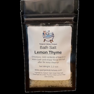 May include: A white resealable pouch with a label that reads "Pampered Chelsea Products Bath Salt Lemon Thyme". The label also includes directions for use, net weight (1.2 ozs), website address, and ingredients. The pouch is filled with white bath salts.