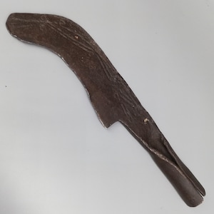 May include: A curved, brown metal tool with a textured surface. The tool has a pointed end and a wider, rounded top. The metal appears to be aged or weathered, with visible imperfections.