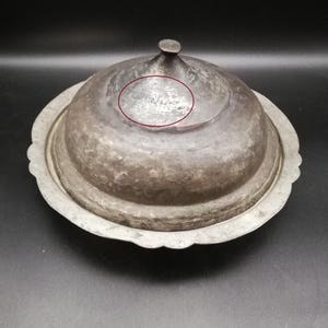 Könnte beinhalten: Eine silberne Servierplatte mit einem gewölbten Deckel. Der Deckel trägt eine Inschrift in arabischer Schrift.