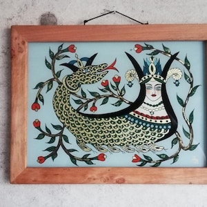 May include: A framed artwork featuring a colorful illustration of a woman with a crown and a dragon-like creature with green scales. The artwork is set against a light blue background with red and green floral accents.