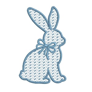 Puede incluir: Un diseño de conejo bordado en azul claro con un lazo. El conejo está relleno con una tela estampada blanca y azul y delineado con una puntada azul claro. El lazo también es azul claro. El diseño está sobre un fondo blanco.