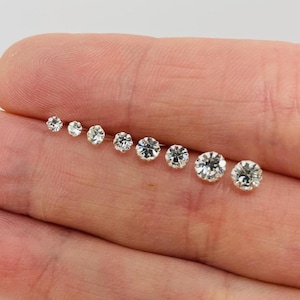 May include: A set of nine clear crystal stud earrings in various sizes, displayed on a hand.