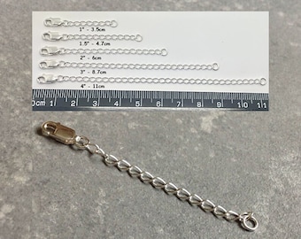 May include: A silver chain extender with a lobster clasp on one end and a jump ring on the other. The extender is shown next to a ruler with measurements in inches and centimeters. The chain extender is available in lengths of 1 inch, 1.5 inches, 2 inches, 3 inches, and 4 inches.