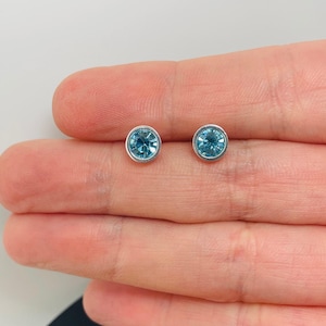 Op de afbeelding: Een paar zilveren oorbelletjes met ronde, lichtblauwe edelstenen.