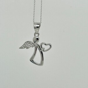 以下が含まれることがあります： ハートのチャームが付いたシルバーのエンジェルペンダントネックレス。エンジェルは小さなハローと、きらめく石のディテールが施された翼を持っています。