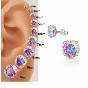 Peut inclure: Boucles d'oreilles à clous rondes avec des cristaux iridescents multicolores montés sur métal argenté. L'image présente un guide des tailles de 2mm à 10mm, montrant les cristaux sur un modèle d'oreille et individuellement avec le poinçon 925.