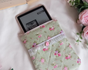 Op de afbeelding: Een gewatteerde, saliegroene e-reader hoes met een bloemenpatroon van roze en paarse rozen. De hoes heeft een witte kanten rand en een klein roze roos accent. Een e-reader is gedeeltelijk zichtbaar in de hoes.