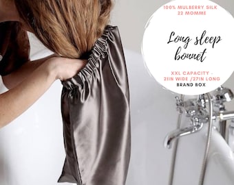 Puede incluir: Un gorro de dormir de seda gris con el texto "Long sleep bonnet" y "XXL Capacity - 21in Wide / 27in Long" y "Brand Box". El gorro está hecho de 100% seda de morera y es de 22 momme.