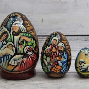 Peut inclure: Trois œufs de Pâques en bois peints à la main représentant une scène de la Nativité. Le plus grand œuf montre Marie, Joseph et l'enfant Jésus. L'œuf du milieu représente les trois rois mages. Le plus petit œuf montre un agneau et une colombe.