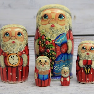 May include: A set of six hand-painted Russian nesting dolls, each depicting Santa Claus. The dolls are primarily red with white accents, featuring detailed faces, beards, and various accessories like clocks and lanterns. The largest doll is about 6 inches tall.