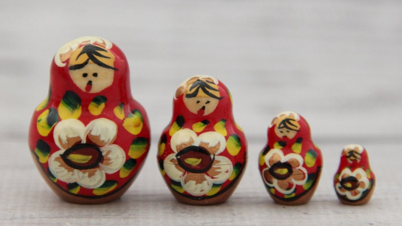 May include: A set of four red Matryoshka nesting dolls. Each doll features a painted floral design with yellow and white petals. The dolls have a wooden appearance and are arranged from largest to smallest.