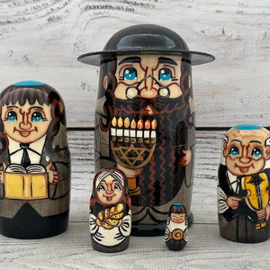 May include: A set of six hand-painted nesting dolls. The largest doll features a man with a beard and a hat, holding a menorah. Other dolls depict figures with books, a violin, and traditional attire. The dolls are painted in shades of brown, black, and blue.