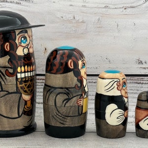 May include: A set of five wooden nesting dolls, each depicting a figure with traditional attire. The largest doll features a man with a black hat and a menorah. The dolls are painted in shades of brown, black, and beige.