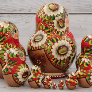 May include: A set of Russian nesting dolls, or Matryoshka dolls, in various sizes. The dolls are painted red with white floral designs, green leaves, and gold accents. The largest doll is about 6 inches tall.