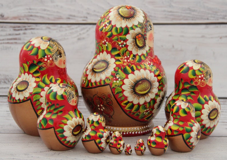 May include: A set of Russian nesting dolls, or Matryoshka dolls, in various sizes. The dolls are painted red with white floral designs, green leaves, and gold accents. The largest doll is about 6 inches tall.