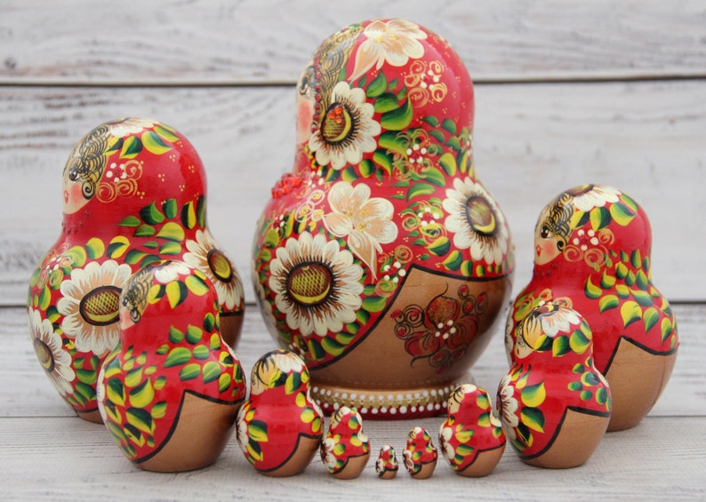 May include: A set of traditional Russian nesting dolls, or Matryoshka dolls, in various sizes. The dolls are painted red with floral and gold accents. The largest doll is approximately 7 inches tall.