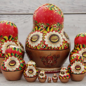 May include: A set of traditional Russian nesting dolls, or Matryoshka dolls, in various sizes. The dolls feature a red background with white sunflower designs and gold and brown accents. The largest doll is approximately 6 inches tall.