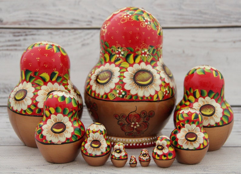 May include: A set of traditional Russian nesting dolls, or Matryoshka dolls, in various sizes. The dolls feature a red background with white sunflower designs and gold and brown accents. The largest doll is approximately 6 inches tall.