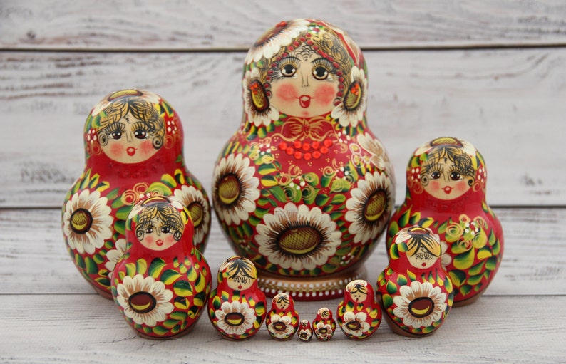 May include: A set of traditional Russian nesting dolls, or Matryoshka dolls, in various sizes. The dolls are painted red with floral and facial details. The largest doll is approximately 7 inches tall.