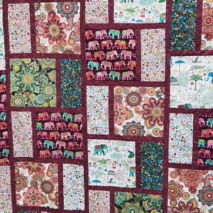 Peut inclure: Une courtepointe compos&eacute;e de diff&eacute;rents carr&eacute;s de tissu pr&eacute;sentant un motif r&eacute;p&eacute;t&eacute; d'&eacute;l&eacute;phants, de paons et de motifs floraux. La courtepointe est r&eacute;alis&eacute;e avec une bordure bordeaux et un fond blanc.