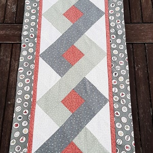 May include: A green and white table runner with a red and white diamond pattern. The runner has a border with a green background and white circles with numbers and Christmas-themed illustrations.