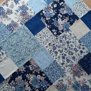 May include: A patchwork quilt with a blue and white floral pattern. The quilt is made up of squares of different fabrics, each with a unique design. The quilt is perfect for adding a touch of elegance to any room.