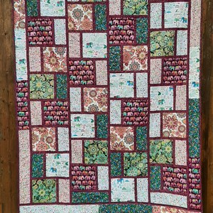 Peut inclure: Une courtepointe patchwork avec un motif g&eacute;om&eacute;trique pr&eacute;sentant diff&eacute;rentes nuances de vert, de rouge et de blanc. La courtepointe est compos&eacute;e de carr&eacute;s et de rectangles avec diff&eacute;rents motifs, notamment des &eacute;l&eacute;phants, des fleurs et des motifs paisley.