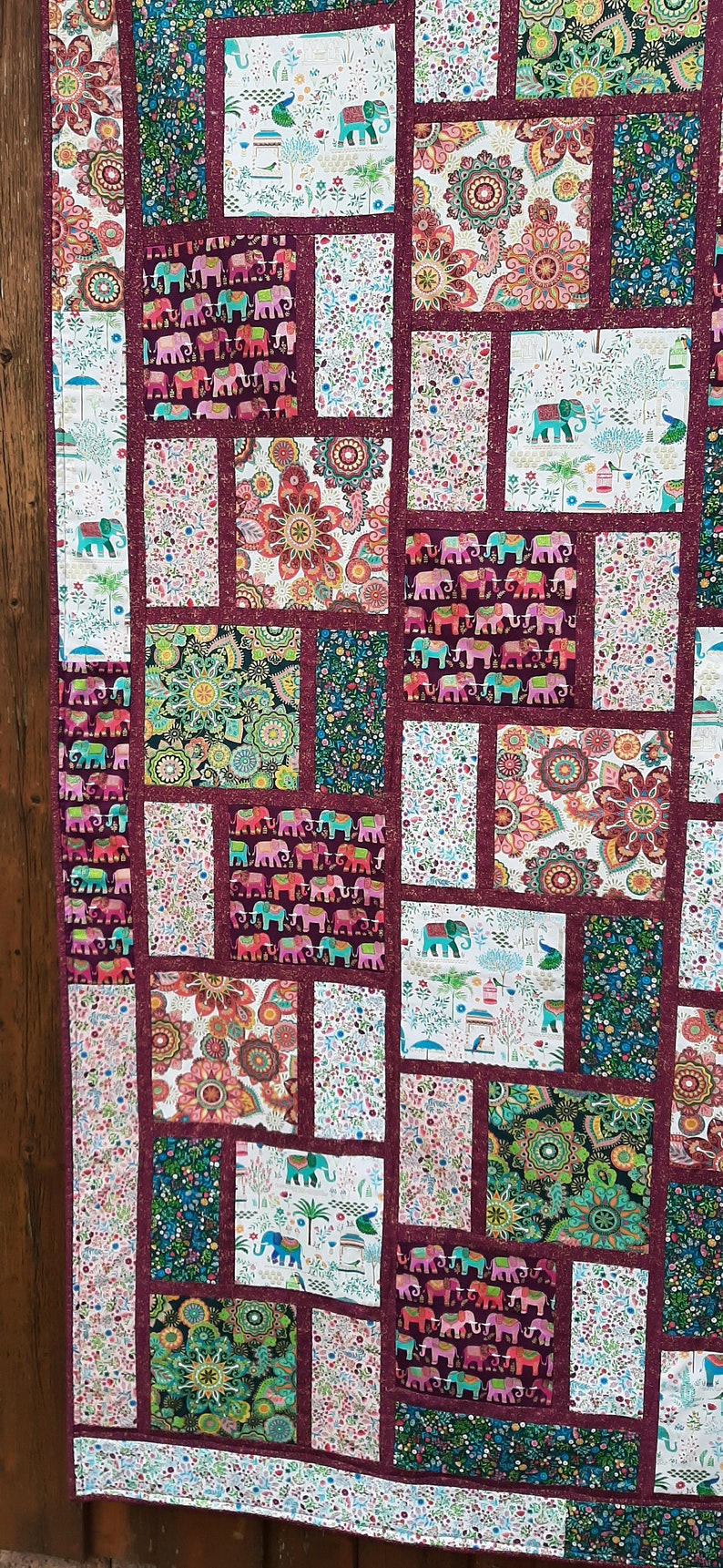 Peut inclure: Une courtepointe en patchwork avec une bordure bordeaux et une vari&eacute;t&eacute; de tissus color&eacute;s repr&eacute;sentant des &eacute;l&eacute;phants, des motifs paisley et des motifs floraux.