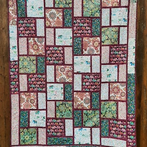 Peut inclure: Une courtepointe color&eacute;e avec un motif de patchwork repr&eacute;sentant des &eacute;l&eacute;phants, des fleurs et des motifs g&eacute;om&eacute;triques. La courtepointe est faite de diff&eacute;rents tissus dans des tons de vert, rouge, blanc et bleu.