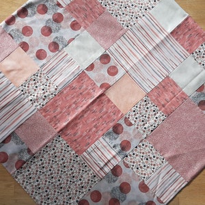 Könnte beinhalten: Ein Patchwork-Deckenstück mit verschiedenen rosa und weißen Stoffen. Die Decke besteht aus Quadraten mit unterschiedlichen Mustern, darunter Streifen, Punkte und Blumenmuster.