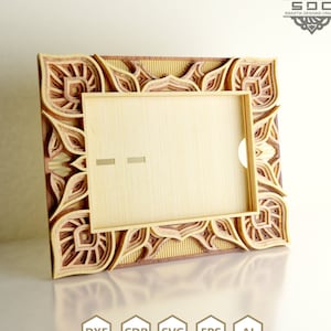 May include: A wooden picture frame with a decorative, intricate design. The frame is made of multiple layers of wood, creating a 3D effect. The frame is in shades of brown and beige.
