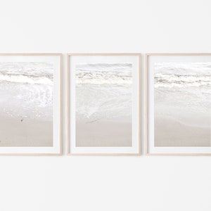 Może przedstawiać: Trzy oprawione wydruki przedstawiające plażę z białymi, pienistymi falami rozbijającymi się o brzeg. Wydruki są w jasnej drewnianej ramie i wiszą na białej ścianie.
