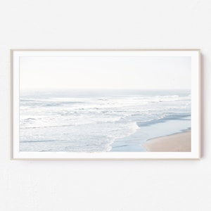 May include: A framed print featuring a serene beach scene. The image captures the ocean waves gently rolling onto the sandy shore. The color palette is soft, with shades of blue and beige, creating a calming and natural aesthetic.