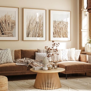 May include: A brown sectional sofa with a light brown throw blanket and pillows with black and white stripes. The sofa is in front of a wall with three framed prints of wheat stalks. The room has a wooden coffee table and a rug with a geometric pattern.