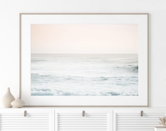 May include: A framed photograph of a seascape with a soft, pale pink sky and blue-green waves. The waves are gently rolling and the water is calm and serene.