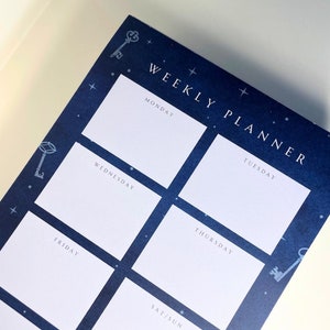 May include: A weekly planner with a dark blue background and white boxes for each day of the week. The days of the week are labelled in white text. The background has a subtle pattern of stars and keys.