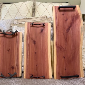 May include: Three wooden serving trays with different handles. The largest tray has a black metal handle, the middle tray has a small branch handle, and the smallest tray has two antler handles. All three trays are made of a reddish-brown wood.
