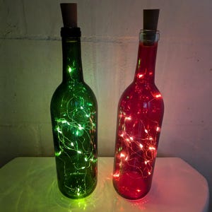 May include: Two glass bottles with cork stoppers, filled with fairy lights. One bottle is green and the other is red.
