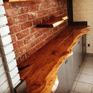 May include: A wooden countertop with a live edge, stained in a rich brown color. The countertop is mounted on gray cabinets and is set against a brick wall.