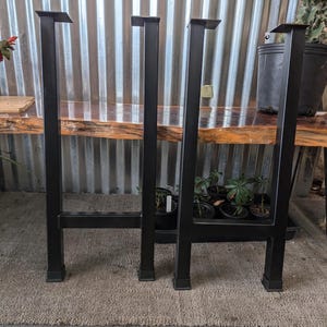 May include: Three black metal table legs with square tops. The legs are standing on a gray carpet.