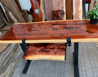 May include: A wooden desk with a live edge top and a black metal frame. The desk has a clear epoxy finish and a smaller shelf underneath.