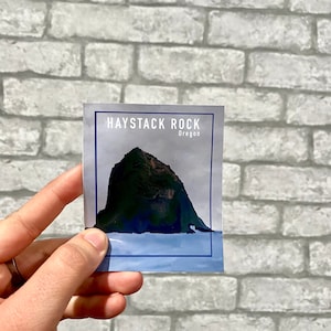 Könnte beinhalten: Eine blaue und weiße Postkarte mit einem Foto von Haystack Rock in Oregon. Der Text auf der Postkarte lautet "Haystack Rock, Oregon".